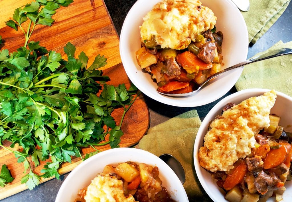 overhead view of 3 bowls of beef stew and a cutting board with fresh fronds of parsley