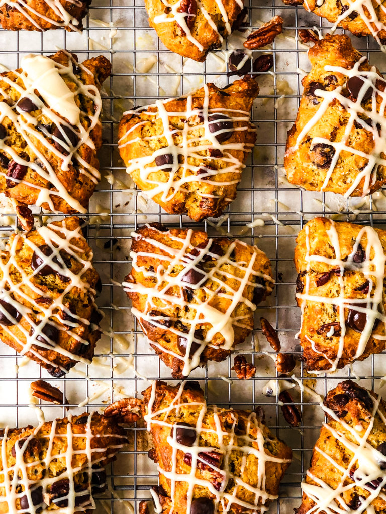 Tray with a dozen Pumpkin Chocolate Chip Scones with streaks of Brown Sugar Glaze, sitting atop baking rack over parchment paper