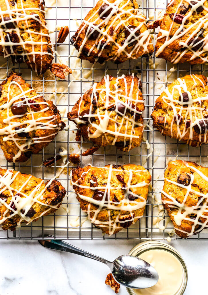 Tray of 9 pumpkin chocolate chip scones with pot of brown sugar glaze with spoon over white marble background