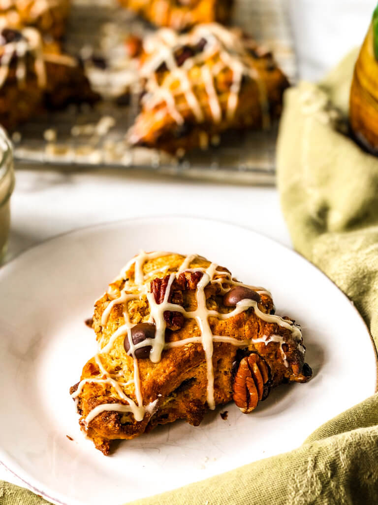 Closeup of Pumpkin Scone drizzled with glaze, with a green napkin at the side and tray of more scones in back