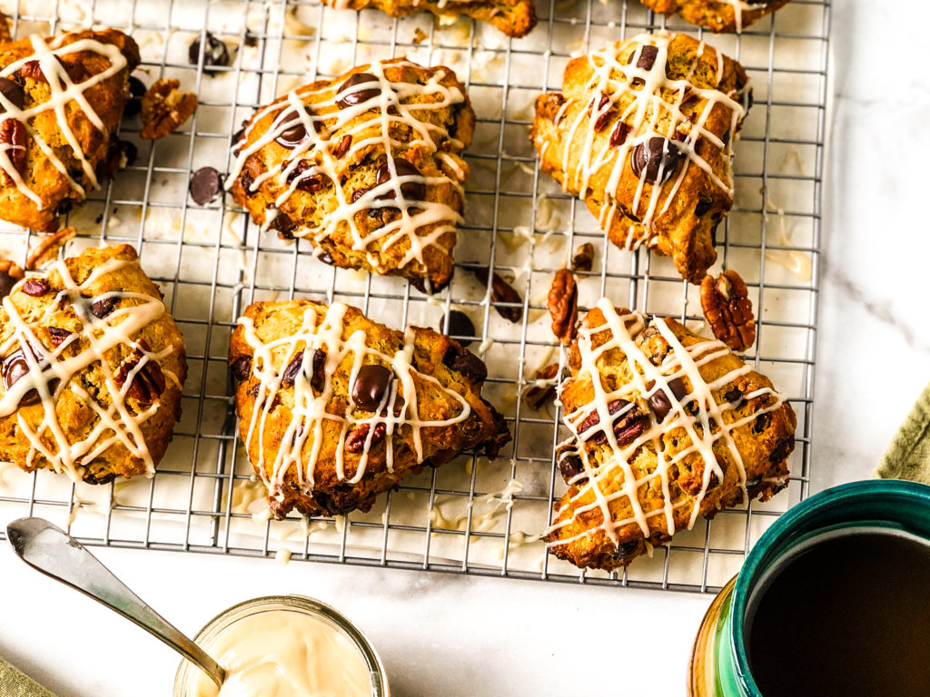 Tray of drizzled scones, showing 6 of them atop a tray, with a small jar of brown sugar glaze and a mug of coffee