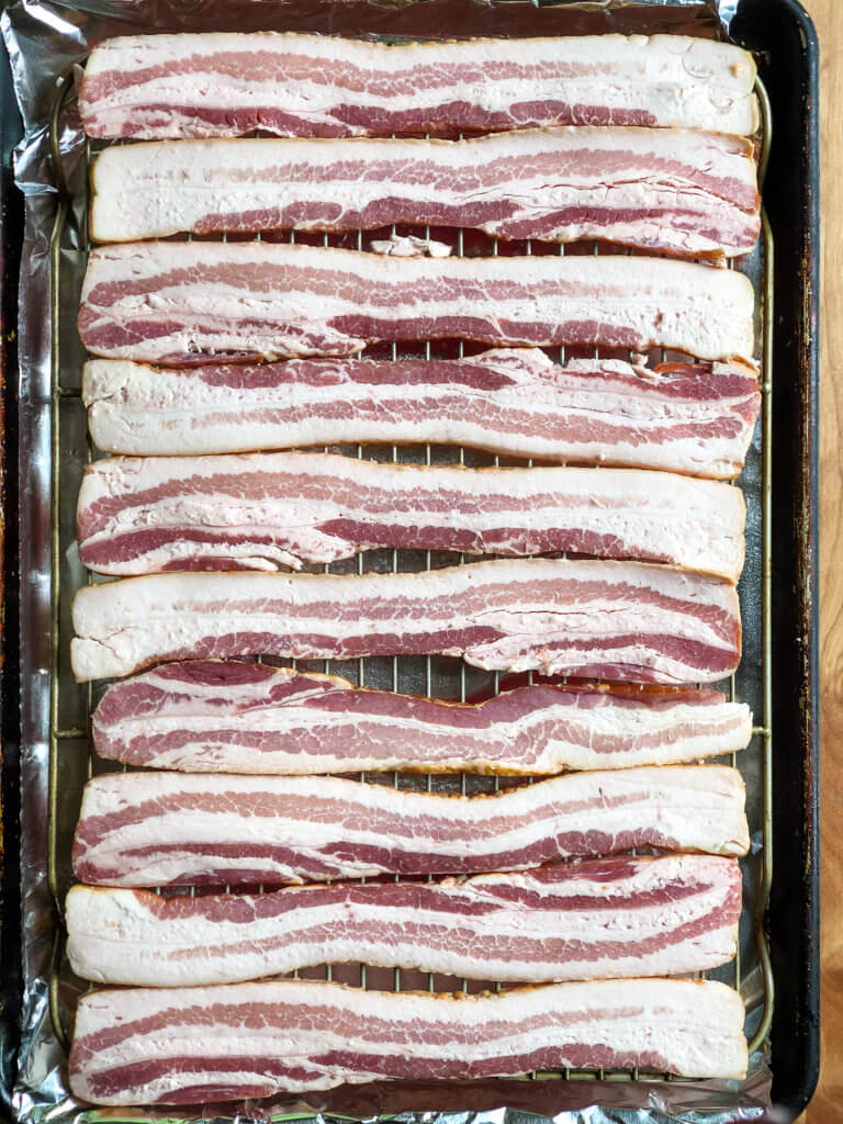 Shows sheet pan of bacon strips laid out over a grate to bake