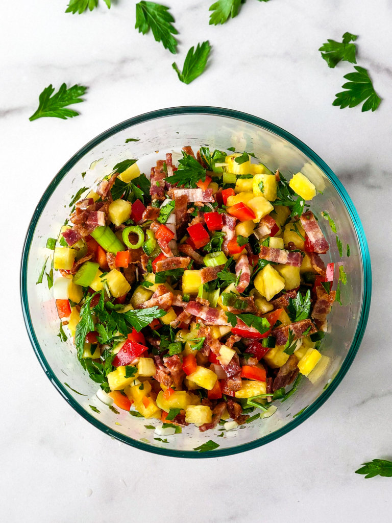 Shows bowl of Pineapple Bacon relish surrounded by parsley leaves