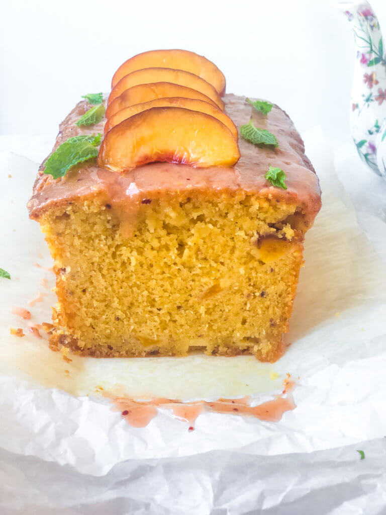 Head-on view of interior of peach lime pound cake. Shows amazing soft firm, small-crumbed texture. Slice peaches lined up with mint leaves on top of cake.