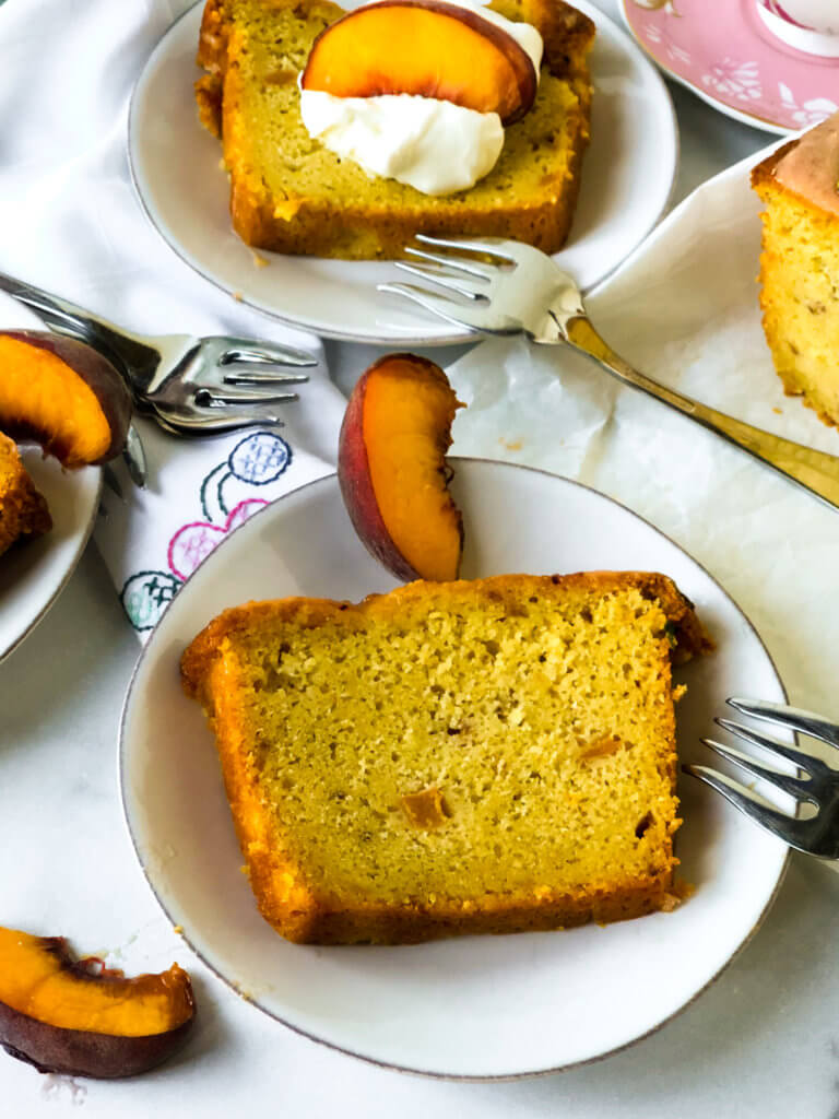 Overhead view of sliced peach lime poundcake. One slis plain, one with whipped cream and peach slice. Peach slices near the plates with corners of other slices seen