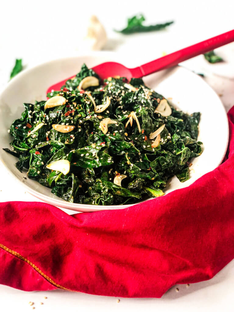 Overhead 45-degree shot of Sautéed Smoky Kale in a bowl, with red serving spoon and a red napkin in front