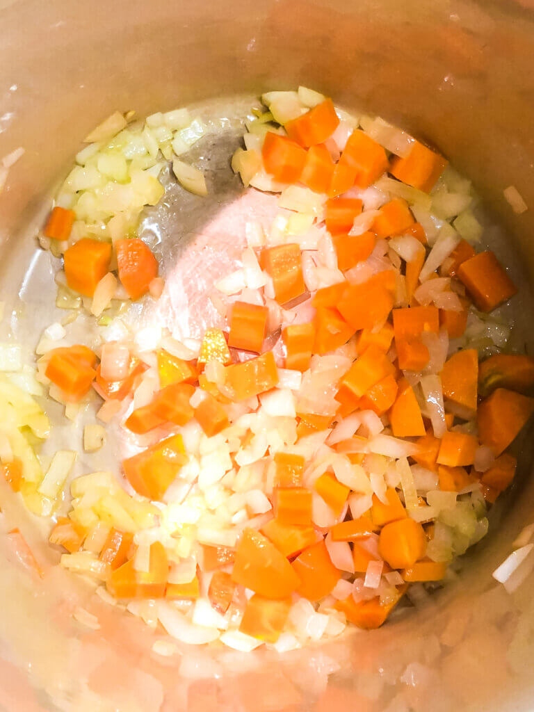 Process shot: Overhead view of carrots and onions sautéing in pan
