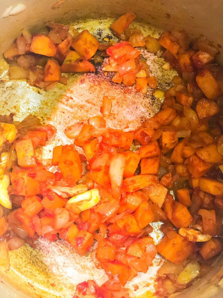 Process shot showing tomato paste in carrot onions sautéing