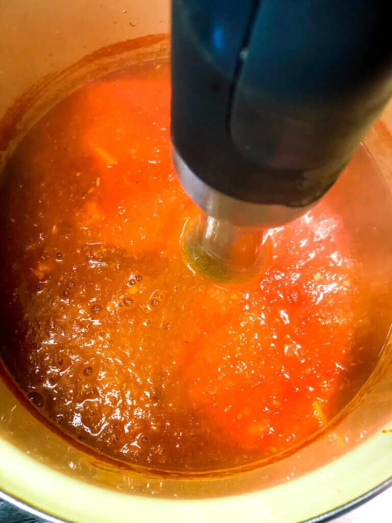 Process shot of immersion blender in tomato white bean soup showing smooth soup