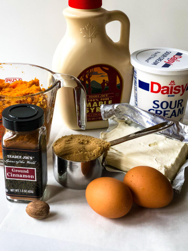 Shows ingredients for sweet potato cheesecake filling: sweet potato, maple syrup, sour cream, cream cheese, eggs, brown sugar, nutmeg, cinnamon