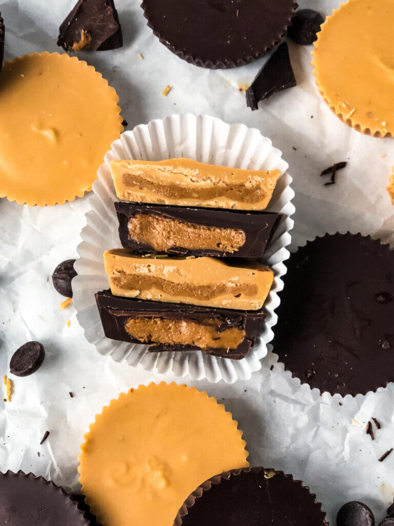 Featured photo showing 4 Pb cup halves, stacked one atop another, with whole peanut butter cups scattered about over white paper