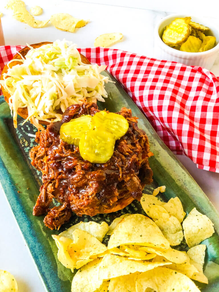 Open-faced BBQ Pulled pork sandwich, topped with pickles and coleslaw. 
