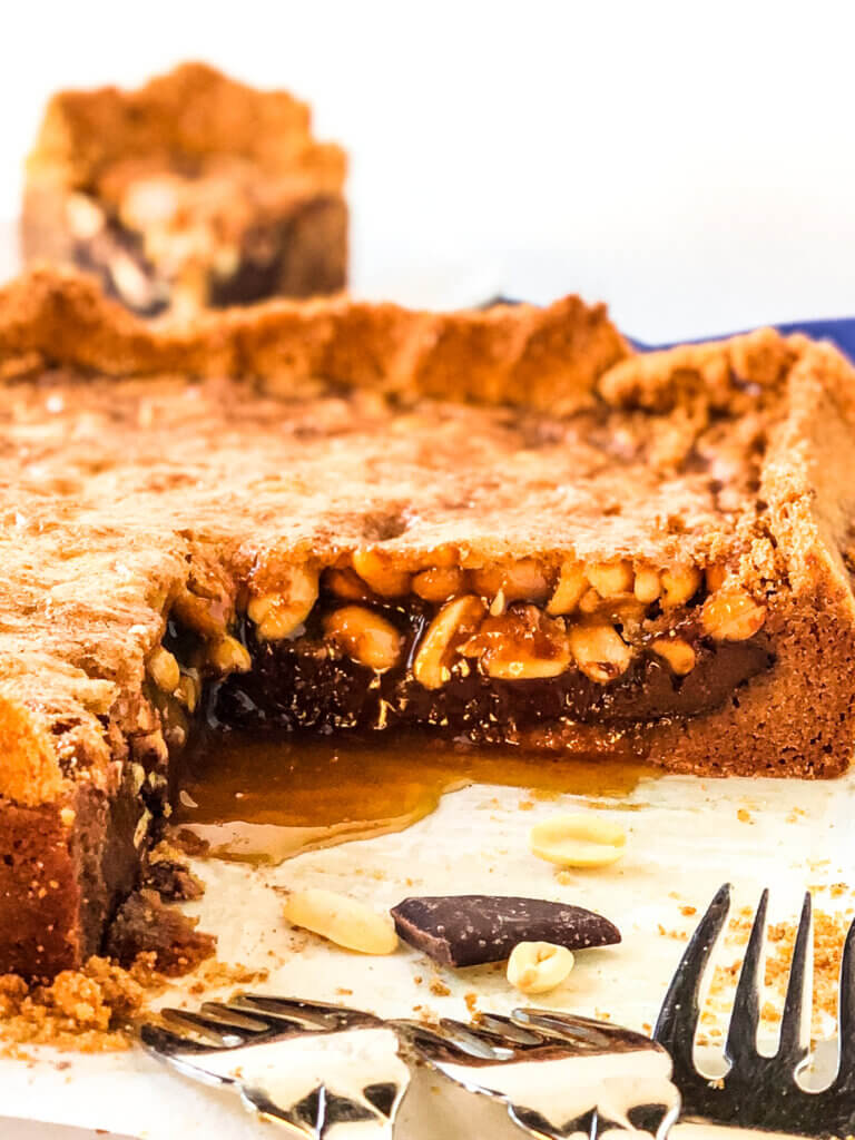 Closeup of the layers in chocolate peanut pie bars, including cookie crust, ganache, caramel sauce and peanuts