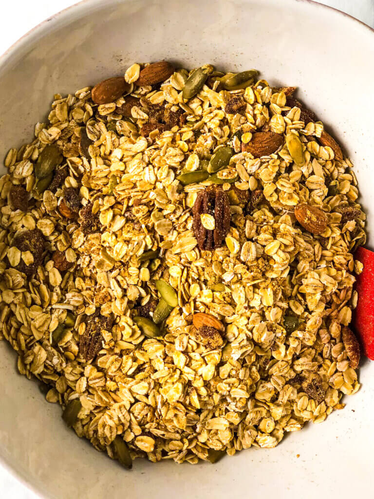 Process shot for Gingerbread Granola Recipe - overhead shot of white bowl holding oats, nuts, spices, ground flaxseed all mixed together