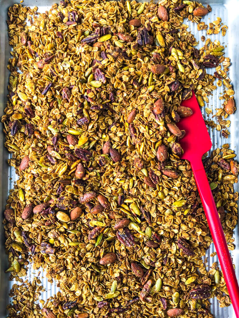 Homemade Gingerbread spiced granola process shot Overhead shot of Baked Gingerbread Granola on sheet pan with red spatula to stir