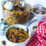 Blog photo showing jar of granola, and ramekin in front and at the side, each containing granola. Toward front is red gingham napkin