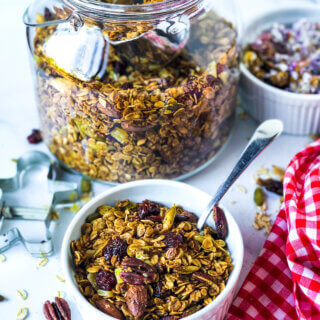 Blog photo showing jar of granola, and ramekin in front and at the side, each containing granola. Toward front is red gingham napkin