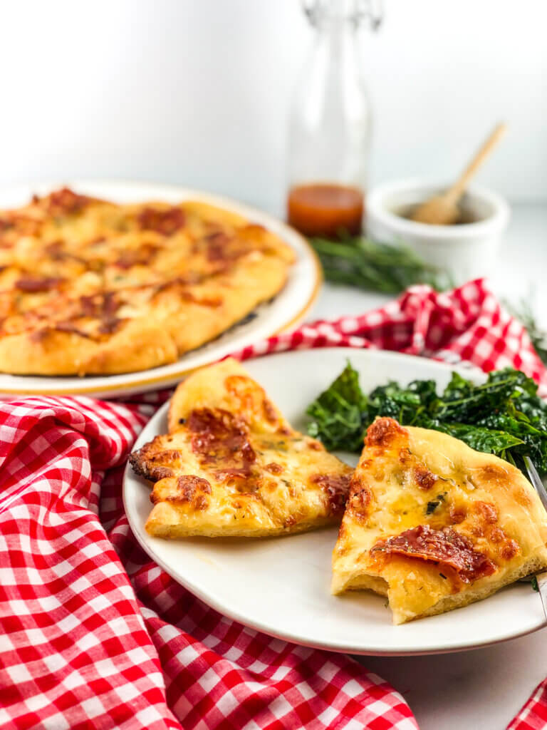 Blog post photo 45-degree view of slices of pizza, drizzled with shimmering honey, with whole pizza in background along with a honey pot and salad dressing cruet