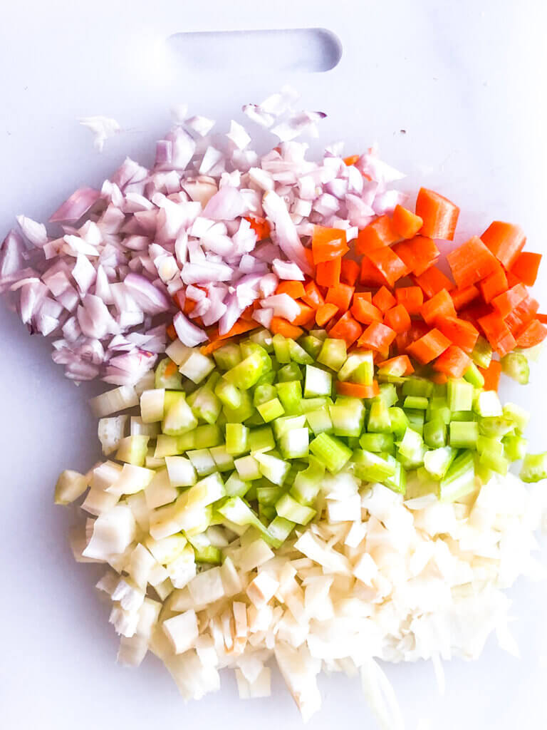 Process shot showing chopped onion, carrot, celery, shallot on white board