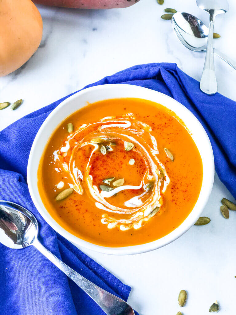 Shows single bowl of sweet potato soup topped with swirl of cream, pepitas and sprinkle of smoked paprika