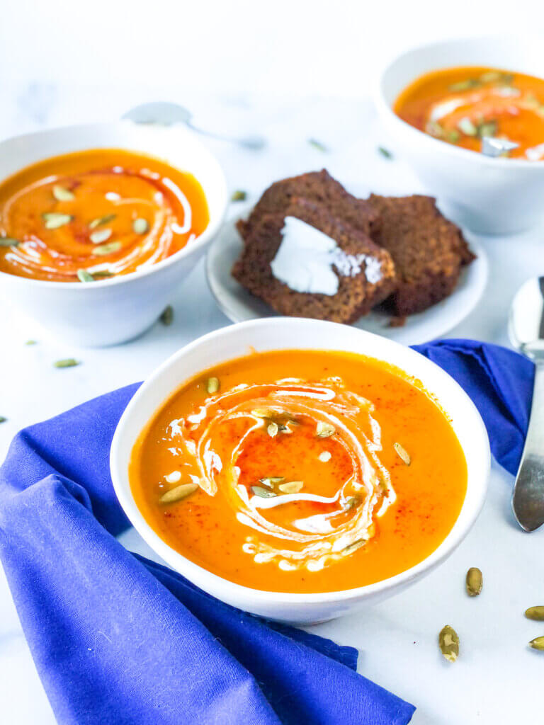 overhead shot of 3 bowls smoky sweet potato soup, each topped with swirl of sour cream, paprika and roasted pepitas