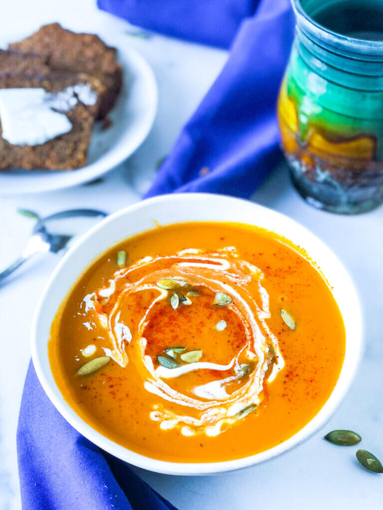 Bowl of sweet potato soup with green mug and plate of buttered brown bread in background. 