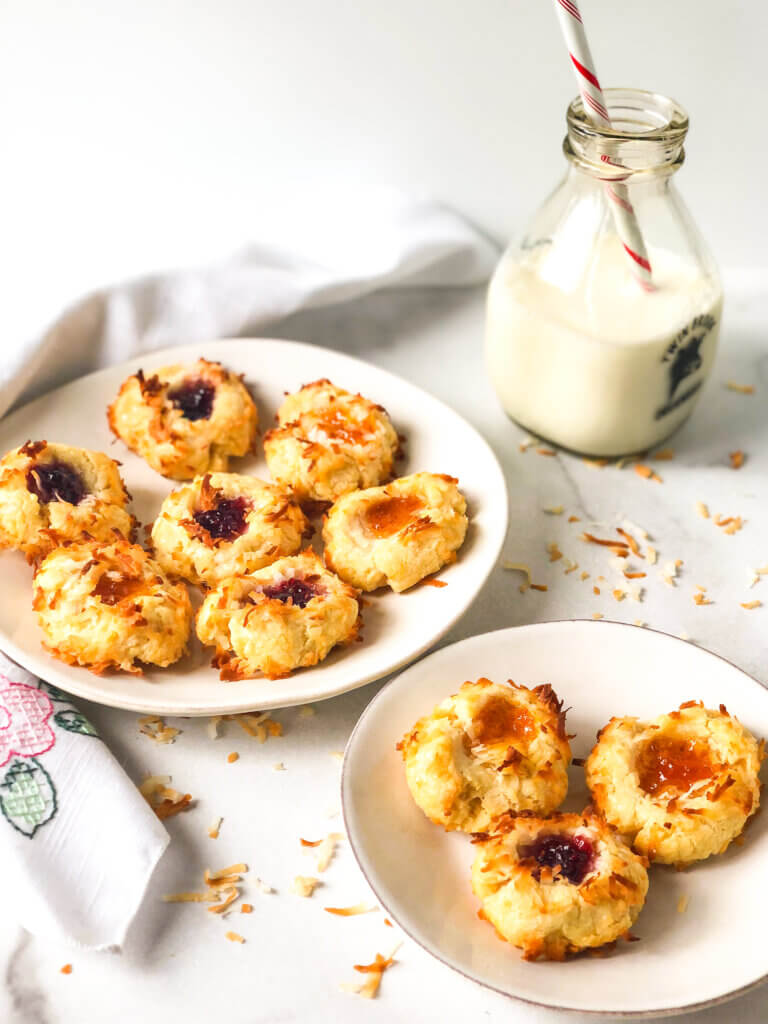 Blog post photo showing a plate of apricot and raspberry coconut-coated thumbprint cookies Bottle of milk with straw, small plate of cookie on white napkin in the white background