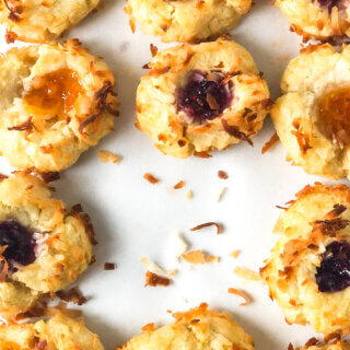 Blog photo showing closeup of grid of apricot and raspberry thumbprint cookies, and scattered toasted coconut