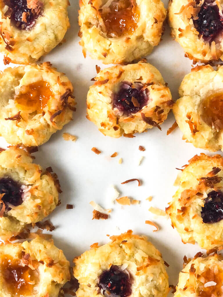 Blog photo showing closeup of grid of apricot and raspberry thumbprint cookies, and scattered toasted coconut