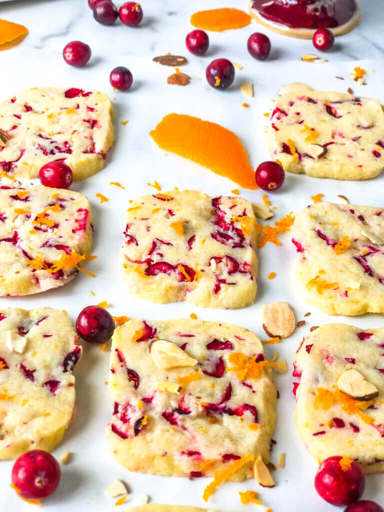 Blog post photo - 45-degree shot showing columns of shortbread cookies, with one missing. Scattered cranberries and orange zest