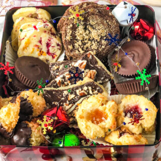 Blog post photo showing Box of Christmas cookies containing cranberry orange shortbread, molasses cookies, peanut butter cups, English toffee, chocolate-dipped macaroons, and jam thumbprints