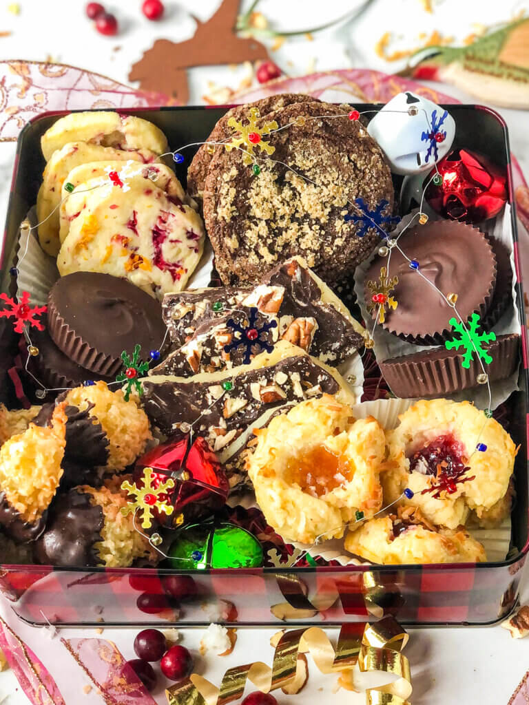 Blog post photo showing Box of Christmas cookies containing cranberry orange shortbread, molasses cookies, peanut butter cups, English toffee, chocolate-dipped macaroons, and jam thumbprints