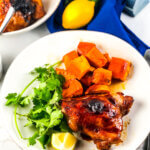 Blog photo showing overhead view of plate of roasted sheet pan maple chicken and sweet potatoes with a lemon wedge, a dish of maple sauce, a lemon and a bowl containing more chicken and sweet potatoes