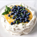 Recipe photo for Pavlova with lemon curd and fresh blueberries. Shows how the lemon curd sits on top of the mascarpone cream and pavlova shell.