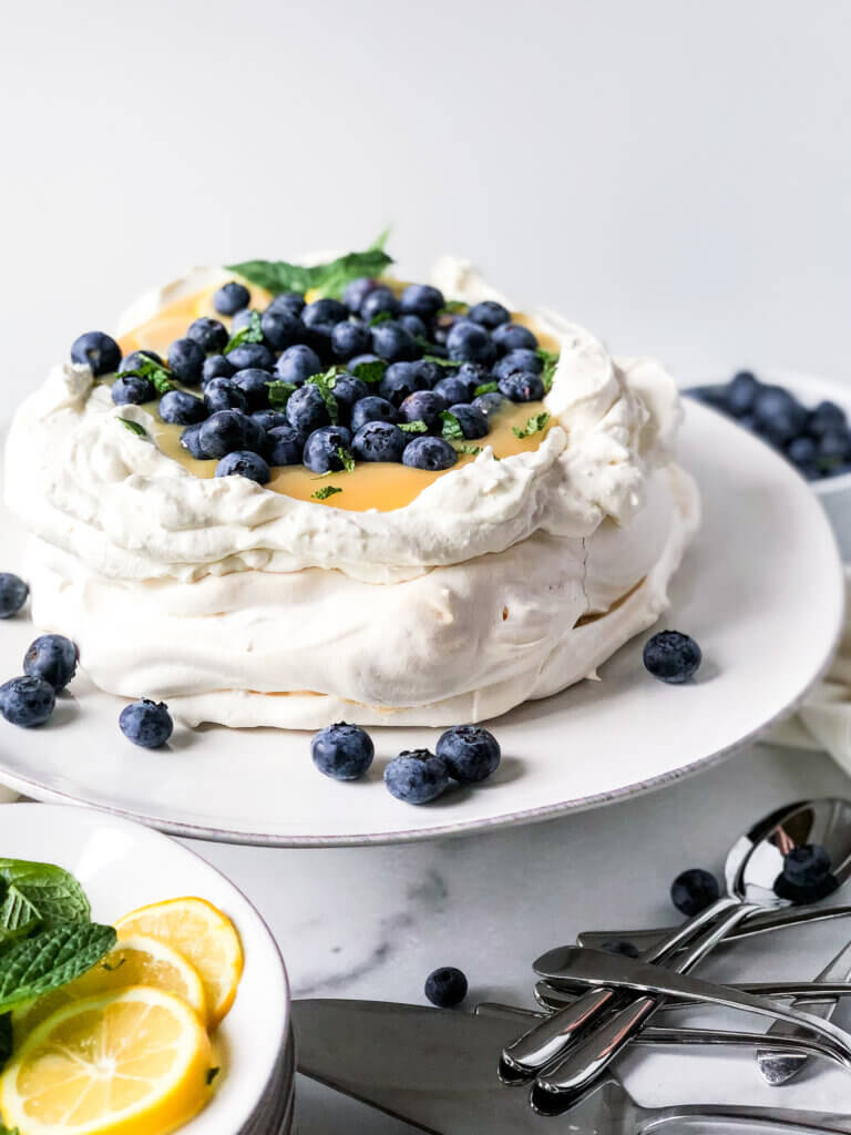 Pavlova with mascarpone cream and filled with lemon curd, sprinkled with blueberries on a white cake plate. 