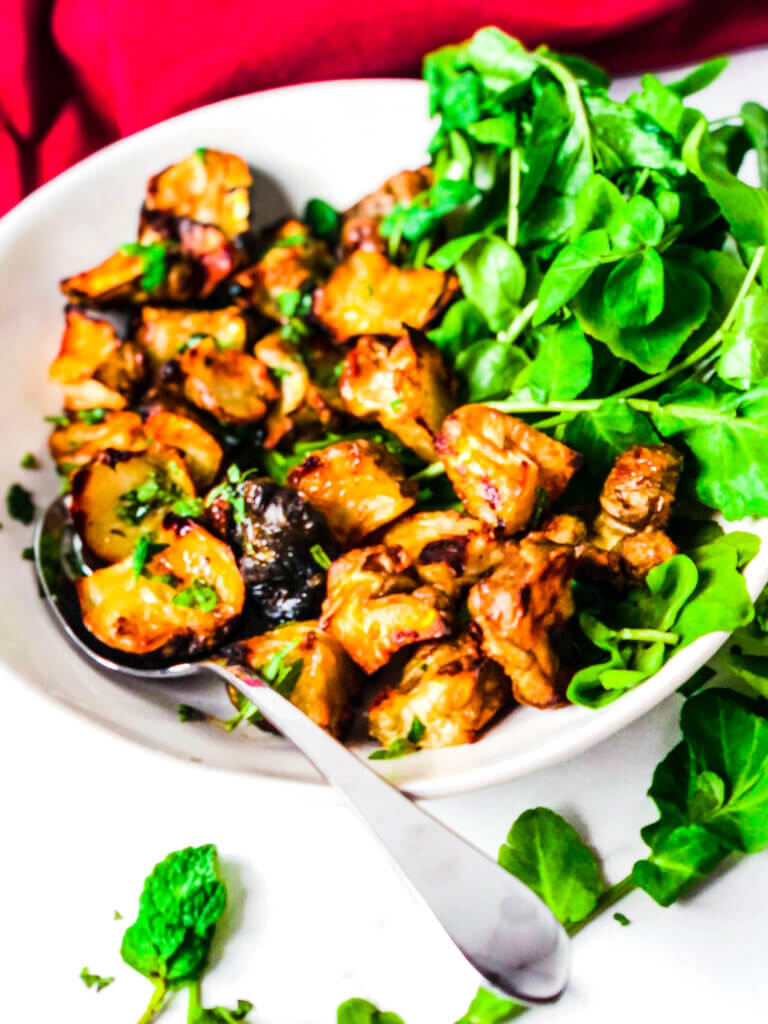 Edges of roasted Jerusalem Artichokes (sunchokes) are deep golden and crispy. Sitting over a bed of greens and sprinkled with fresh basil and mint leaves.