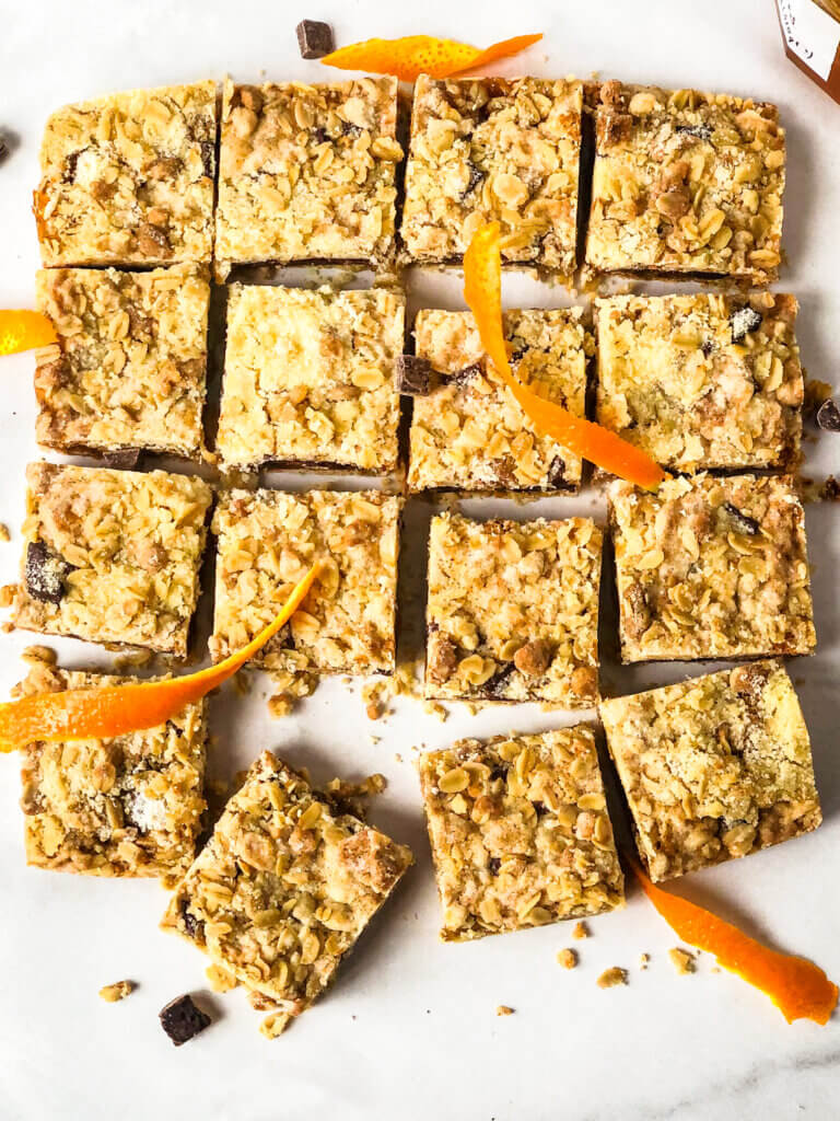 16 Oat bars in grid with several angled outward at the bottom, scattered chocolate pieces and orange rind