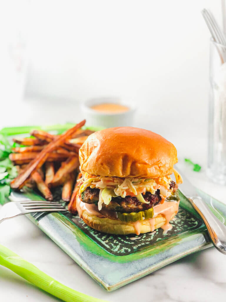 Pork Burger and fries on a green plate, a bowl of burger/fry sauce in all-white background