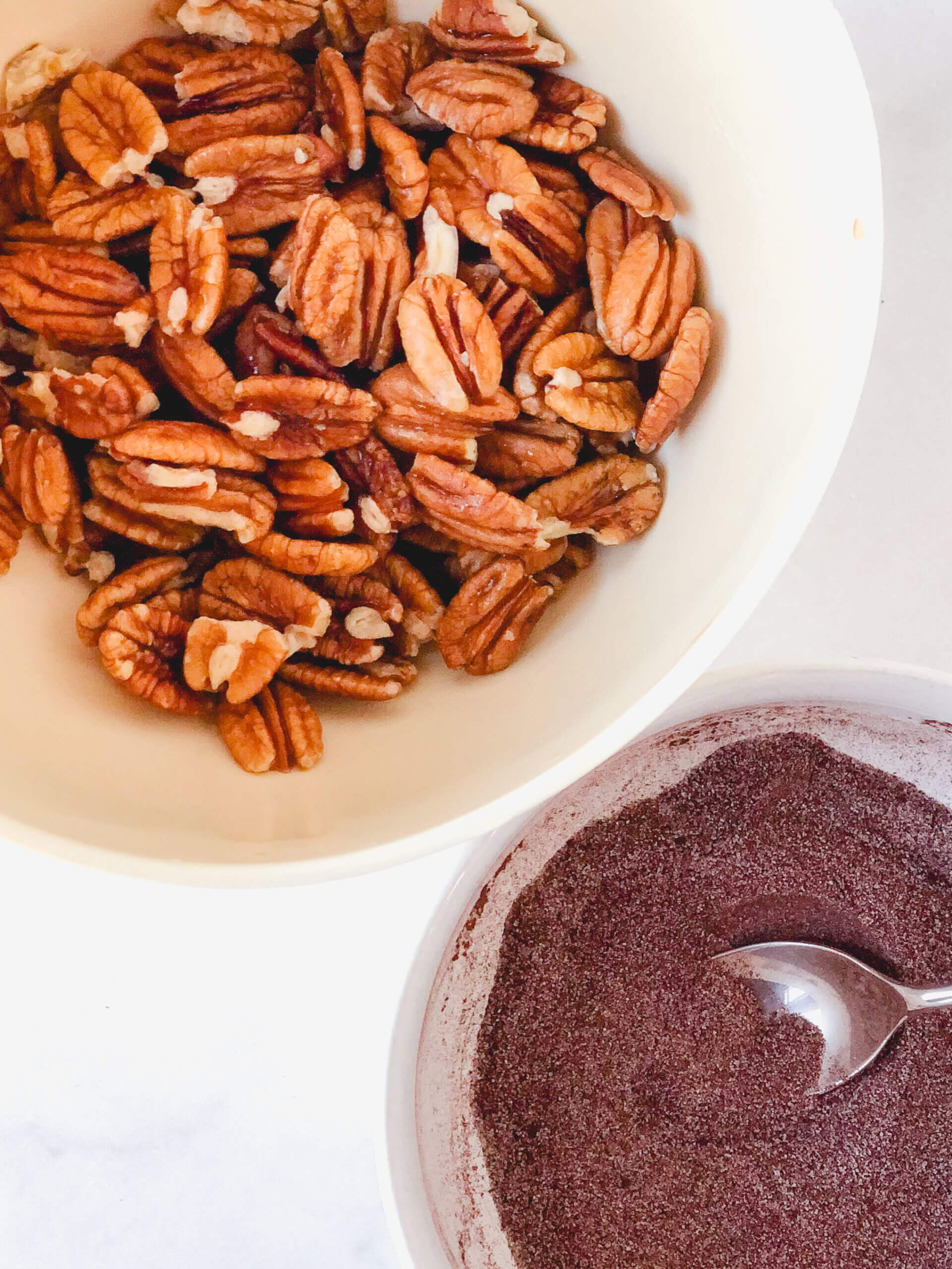 Overhead view showing drained pecans in a bowl, next to bowl with mixed up spices