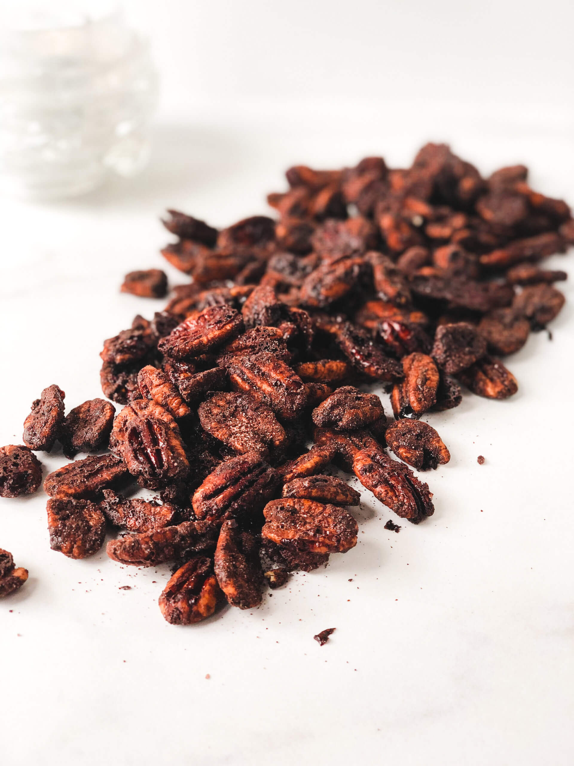 Roasted Spicy Cocoa Pecans poured over white surface in a diagonally-oriented pile. Shows how toasty and cocoa-y they are