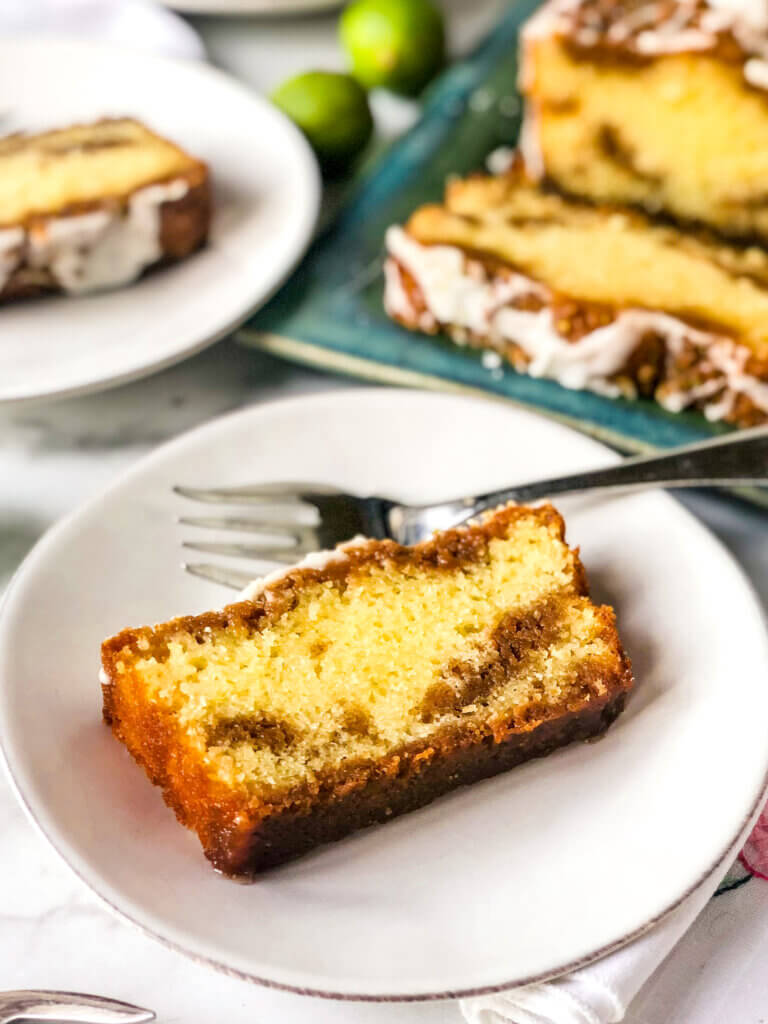 Cross section of key lime cake slice, with layers of cake and graham cracker streusel. Full loaf and another slice in background