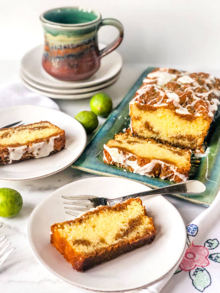 Shows the graham swirl in a slice of key lime pound cake. The rest of the cake in background with a cup of coffee