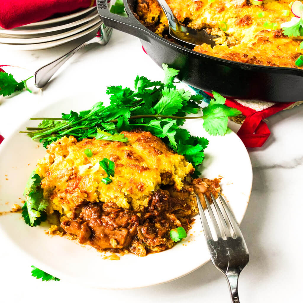 crispy golden-yellow Chicken in Mole sauce, topped with crispy corn crust. Background has castiron pan full of casserole.