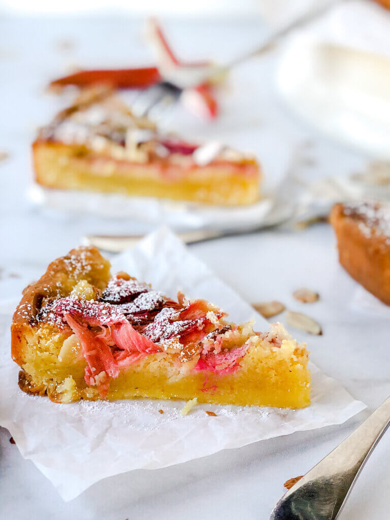 Closeup of rhubarb frangipane tart showing strips of pink rhubarb and almond filling all tucked into shortbread crust